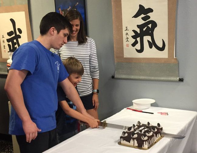 Instructor helps student cut birthday cake with a sword